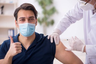 Genç erkek hasta yaşlı erkek doktoru aşıyla ziyaret ediyor.