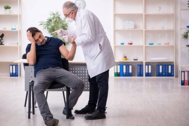 Genç erkek hasta yaşlı erkek doktoru aşıyla ziyaret ediyor.