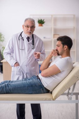 Genç erkek hasta yaşlı erkek doktoru ziyaret ediyor.