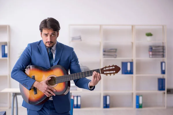 Joven empleado masculino tocando guitarra en el lugar de trabajo — Foto de Stock