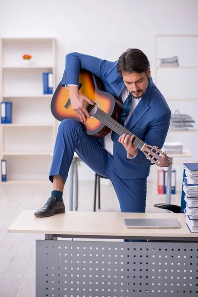 Young male employee playing guitar at workplace — Stock Photo, Image