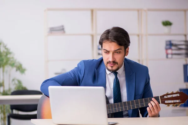 Jeune employé masculin jouant de la guitare sur le lieu de travail — Photo