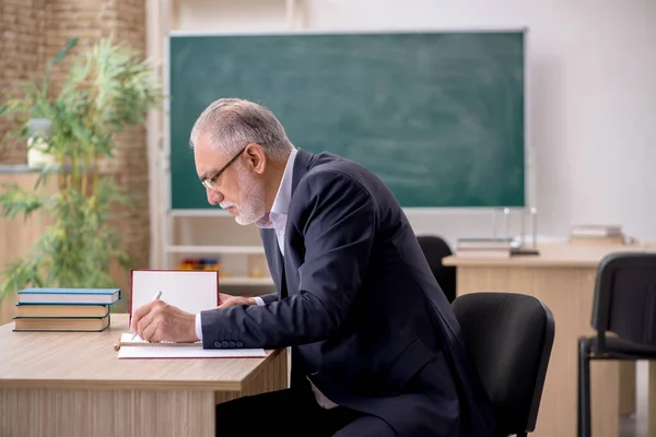 Old male teacher in front of blackboard