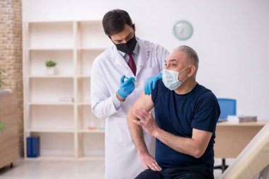 Yaşlı bir erkek hasta aşıyla genç bir doktoru ziyaret ediyor.