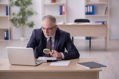 Eski erkek çalışan işyerinde oturuyor.