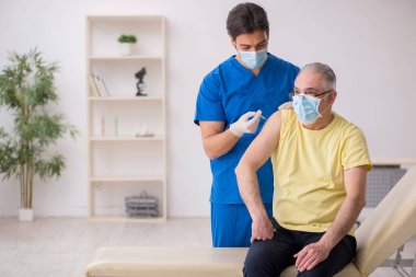 Yaşlı erkek hasta aşılama bölümünde genç bir erkek doktor.