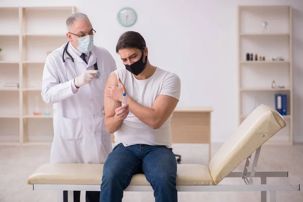 Mladý pacient mužského pohlaví navštěvující starého lékaře v vakcinačním konceptu — Stock fotografie