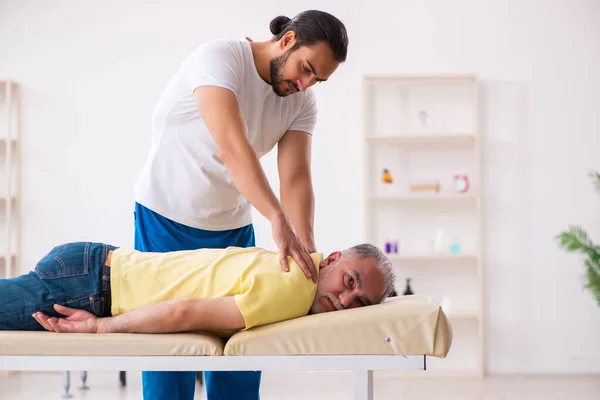 Vecchio paziente maschio visita giovane medico chiropratico maschile — Foto Stock