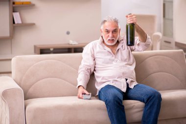 Yaşlı adam evde alkol içiyor.