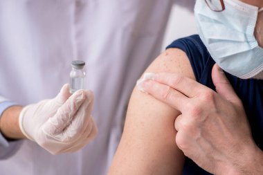 Yaşlı bir erkek hasta aşıyla genç bir doktoru ziyaret ediyor.