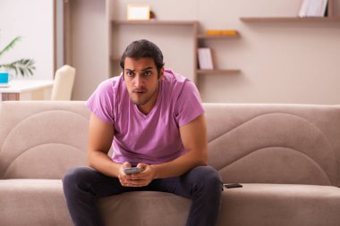 Genç adam salgın sırasında evde televizyon izliyor.