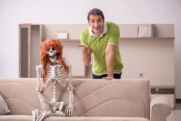 Молодой человек сидит на диване с женским скелетом — стоковое фото