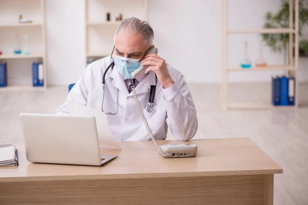 Yaşlı erkek doktor salgın sırasında klinikte çalışıyor. — Stok fotoğraf