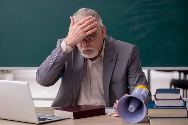 Gammal manlig lärare som håller megafon framför svarta tavlan — Stockfoto