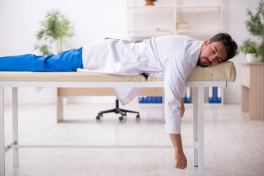 Hastanede kanepede yatan yorgun genç bir erkek doktor.