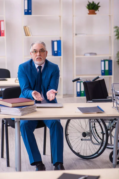 Gammal manlig anställd i rullstol sitter på kontoret — Stockfoto