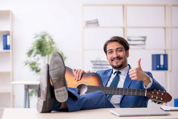 Joven empleado masculino tocando guitarra en el lugar de trabajo —  Fotos de Stock