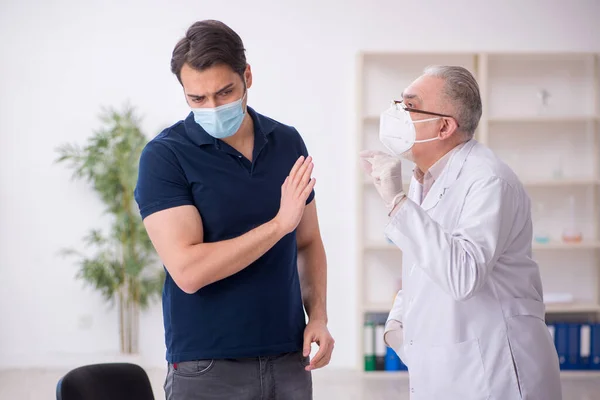 Genç erkek hasta salgın sırasında yaşlı erkek doktoru ziyaret ediyor. — Stok fotoğraf