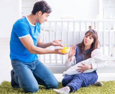 Yeni doğmuş bebekleriyle halıda oturan genç ebeveynler.