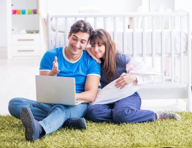 Yeni doğmuş bebekleriyle halıda oturan genç ebeveynler.