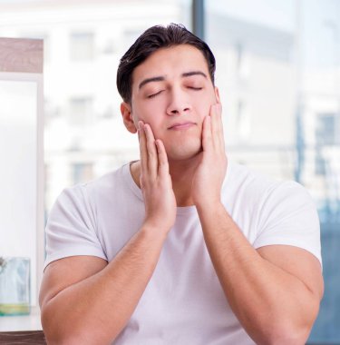 Genç yakışıklı adam yüz kremi sürüyor.