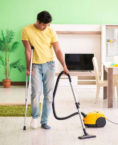 Gewond man op krukken stofzuigerhuis — Stockfoto