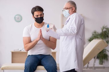 Genç erkek hasta aşı konseptinde yaşlı doktoru ziyaret ediyor.