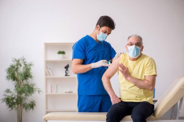 Yaşlı erkek hasta aşılama bölümünde genç bir erkek doktor.