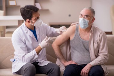 Genç erkek doktor aşı konseptinde yaşlı hastayı ziyaret ediyor.