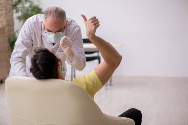 Genç erkek hasta yaşlı doktor otorhinolaryngologis 'i ziyaret ediyor.