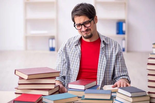 Jonge mannelijke student en te veel boeken in de klas — Stockfoto