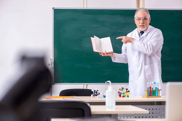 Old male teacher chemist in the classroom