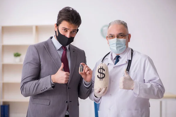 Jonge zakenman bezoekt oude mannelijke arts in vaccinatie concep — Stockfoto