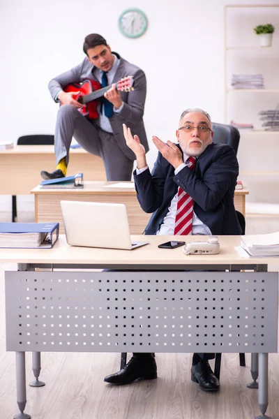 Young male employee playing guitar in the presence of old boss — Stock Photo, Image