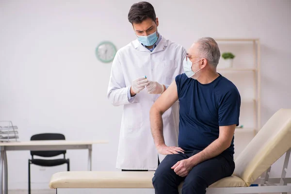 Starý mužský pacient na návštěvě mladý mužský lékař v vakcinaci conce — Stock fotografie