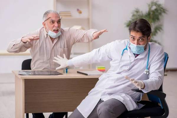 Idős férfi beteg, aki fiatal férfi orvost látogat a világjárvány idején — Stock Fotó
