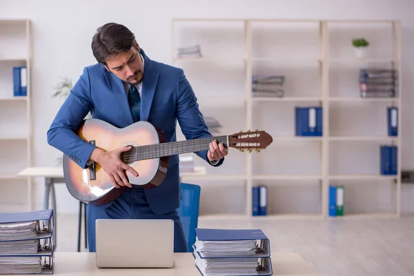 Jovem funcionário do sexo masculino tocando guitarra no local de trabalho — Fotografia de Stock