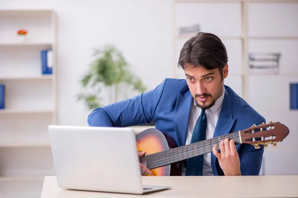 Jovem funcionário do sexo masculino tocando guitarra no local de trabalho — Fotografia de Stock