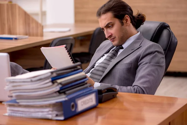 Young male employee and too much work in the office — Stock Photo, Image