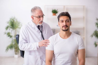 Genç erkek hasta yaşlı erkek doktoru ziyaret ediyor.