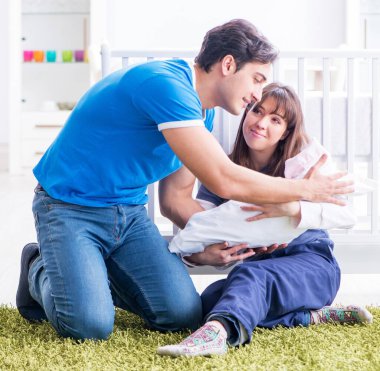 Yeni doğmuş bebekleriyle halıda oturan genç ebeveynler.