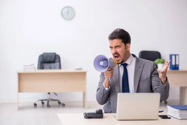 Joven empleado masculino sosteniendo megáfono en el lugar de trabajo —  Fotos de Stock