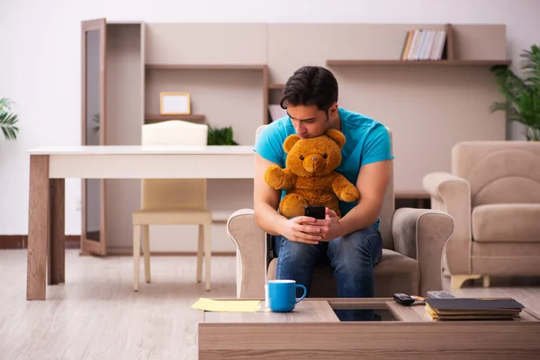 Jovem sentado com urso brinquedo em casa — Fotografia de Stock