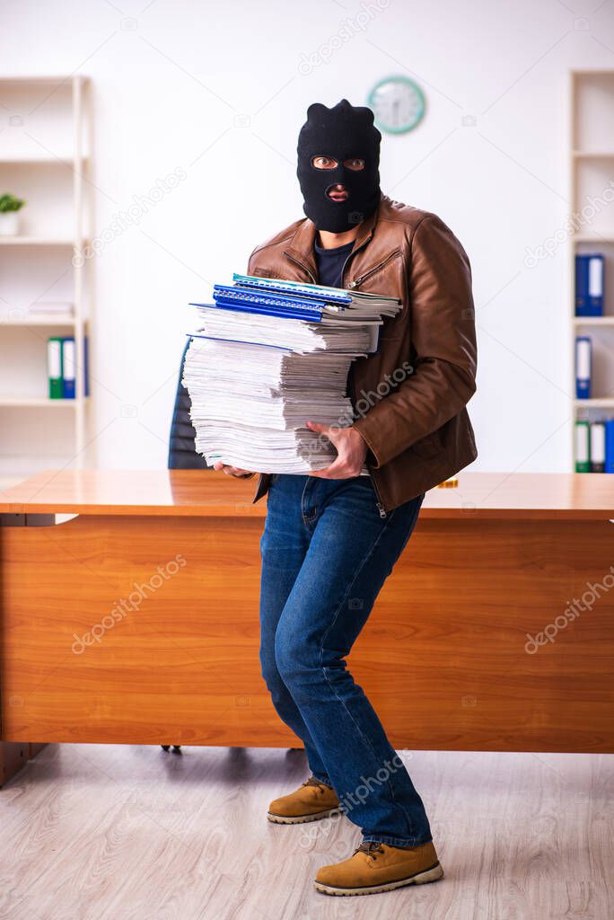 Young man in balaclava stealing information from the office