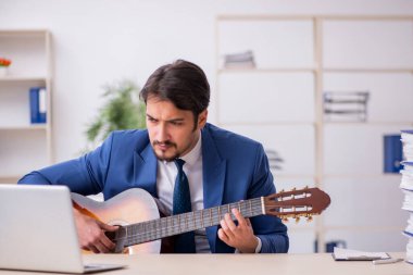 Genç erkek çalışan işyerinde gitar çalıyor.