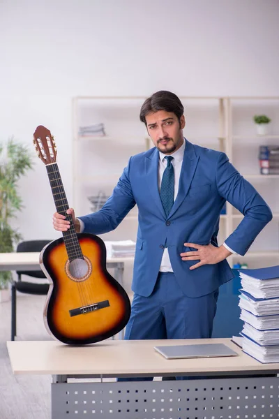 Ung manlig anställd spelar gitarr på arbetsplatsen — Stockfoto