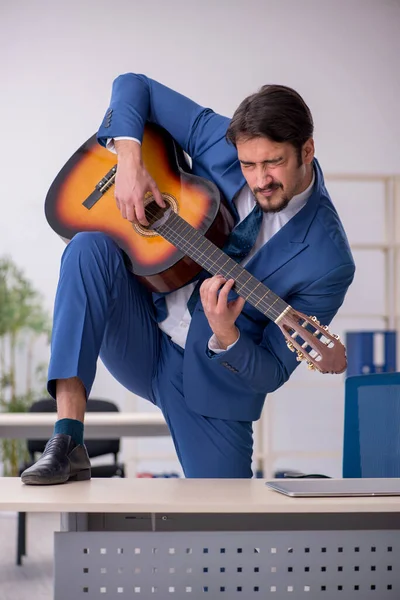 Young male employee playing guitar at workplace — Stock Photo, Image