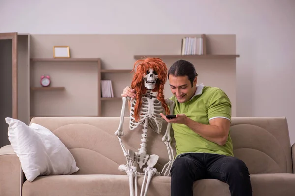 Jovem sentado no sofá com esqueleto feminino — Fotografia de Stock