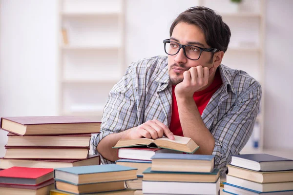 Fiatal férfi diák és túl sok könyv az osztályteremben. — Stock Fotó
