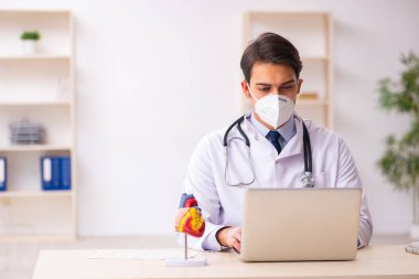 Genç erkek doktor kardiyolog pand sırasında klinikte çalışıyor.